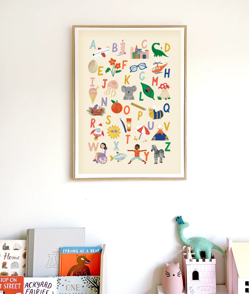 Framed children's alphabet poster by Lauren Sissons with colorful illustrations corresponding to each letter, including animals, objects, and playful scenes on a beige background.