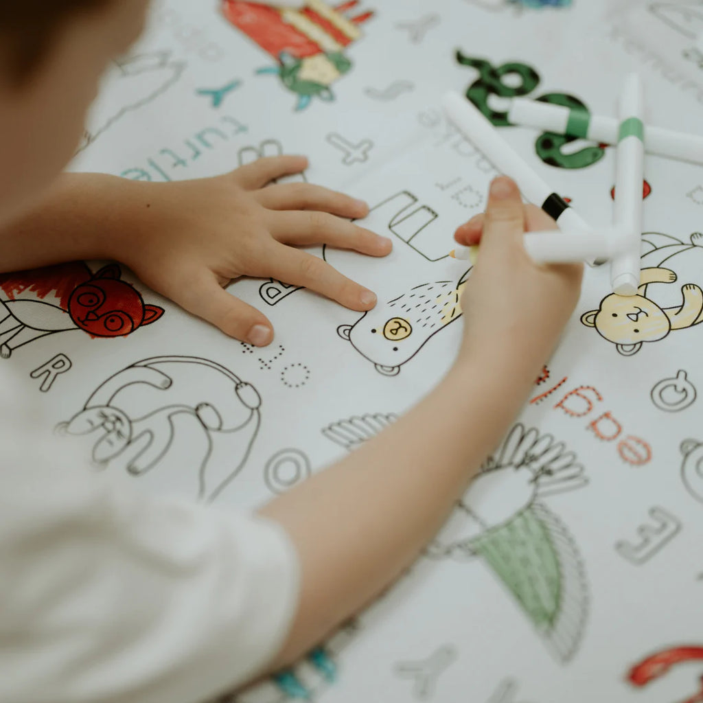Zoomed-in view of hands colouring alphabet-themed animal drawings on the reusable tablecloth—great for letter recognition and creativity.