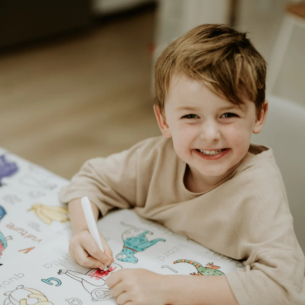 Child smiling while colouring the Alphabet Animals reusable tablecloth, showcasing fun and educational screen-free play.