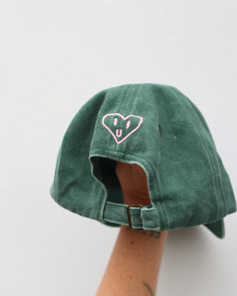 Back view of green "Hands Full Heart Full" cap showing heart embroidery and brass adjustable strap.