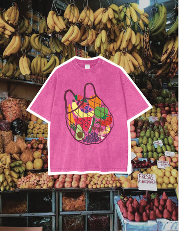Magenta pink oversized women’s t-shirt with colourful fruit market graphic print, laid flat against a fruit stand backdrop