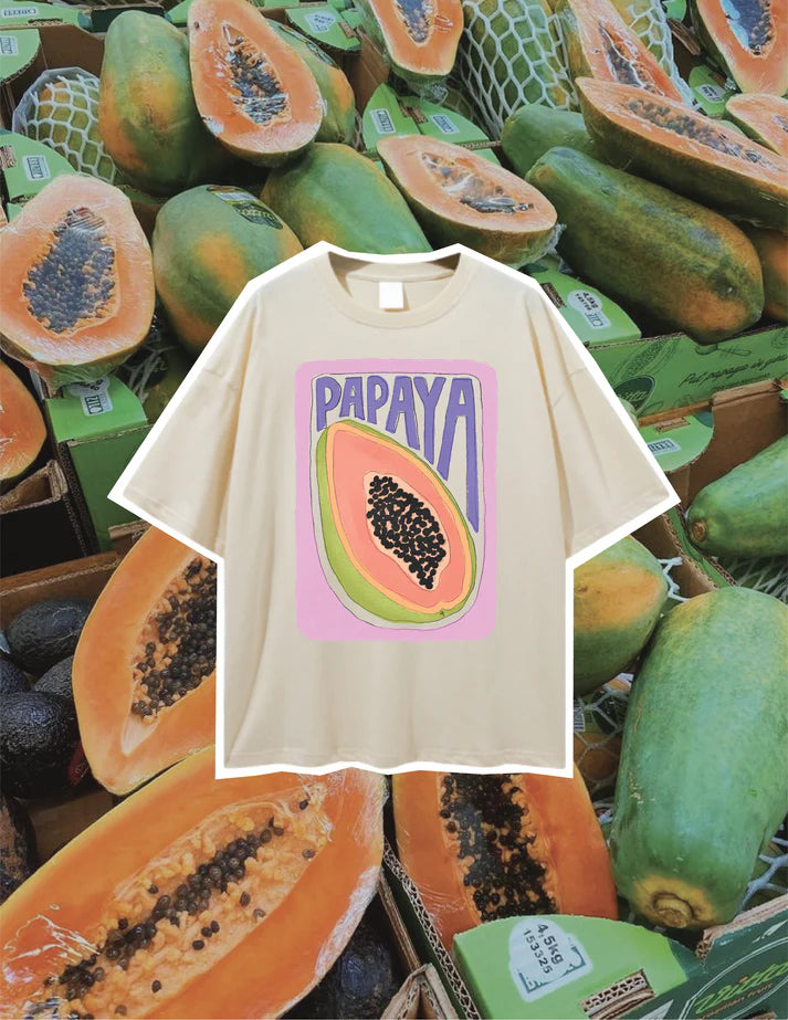 Butter yellow oversized women’s t-shirt with papaya graphic print, laid flat on a display of fresh papayas