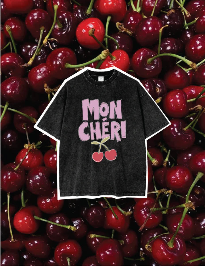 Washed charcoal oversized women’s t-shirt with pink ‘Mon Chéri’ cherry graphic, laid flat on a bed of fresh cherries