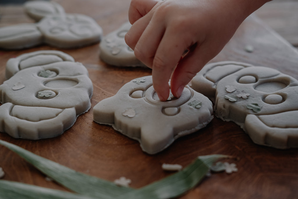 Hand arranging playdough aussie animal shapes on a wooden surface