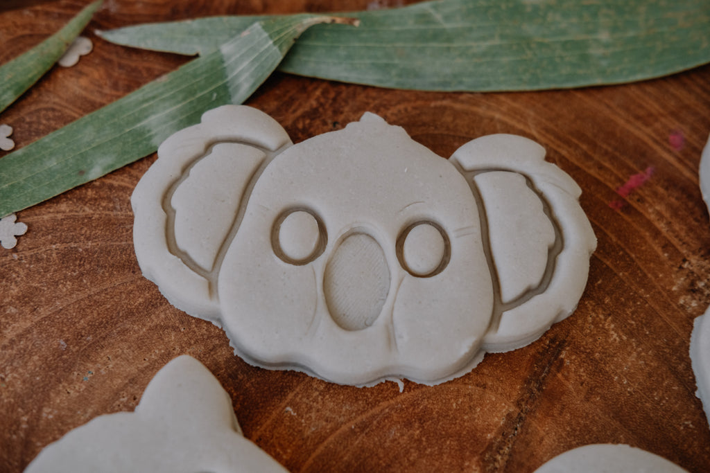 Playdough shaped like a koala on a wooden surface with green leaves.