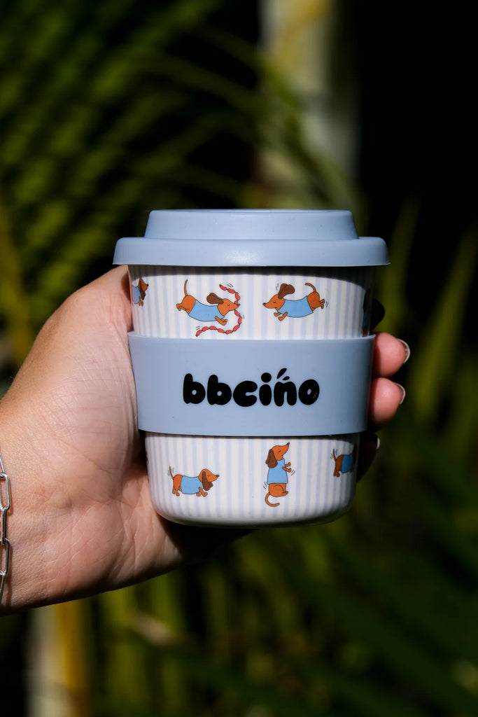 Hand holding BBCino reusable cup 240ml in Dash in Blue dachshund design with blue silicone lid, lightweight eco-friendly coffee cup