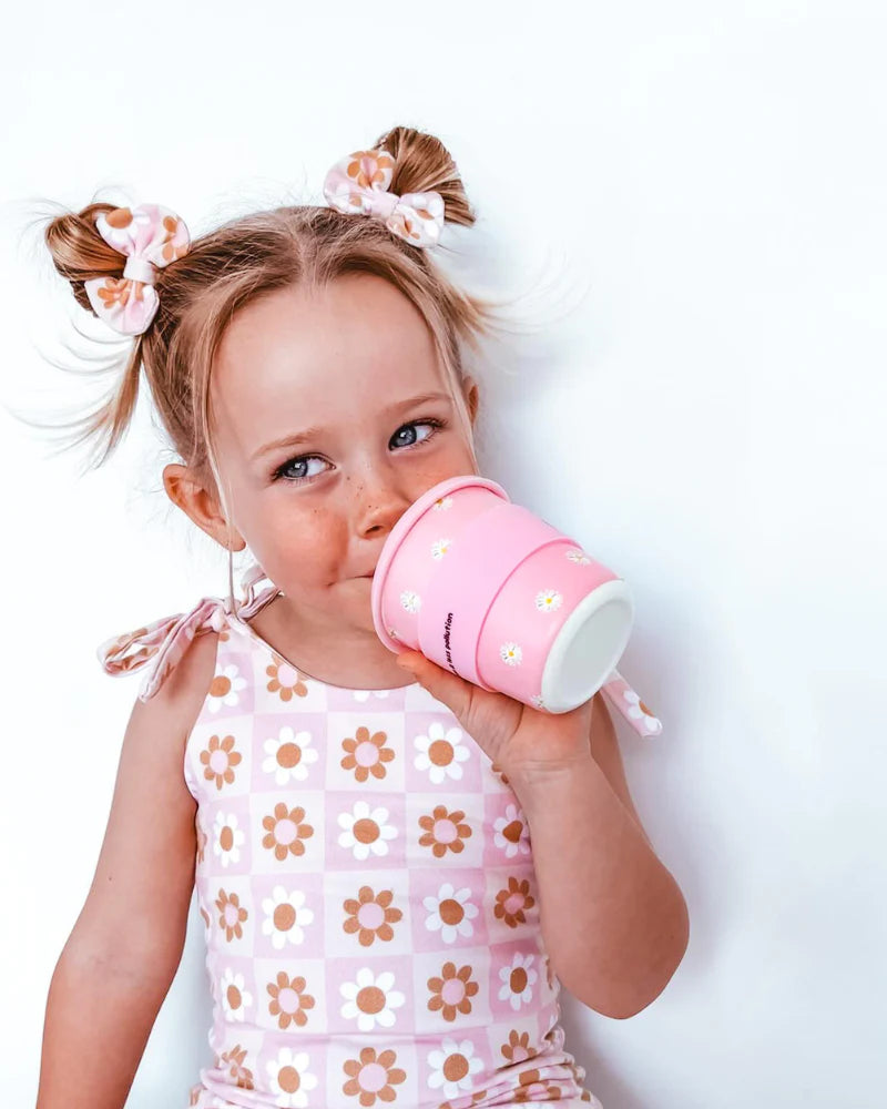 Young girl drinking from a BambinoCino pink reusable cup with daisy print and yellow straw.