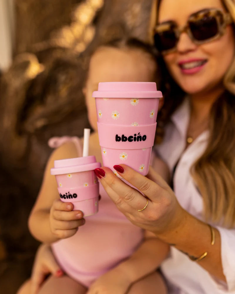Woman and child holding light pink reusable cups with daisy print while smiling outdoors.