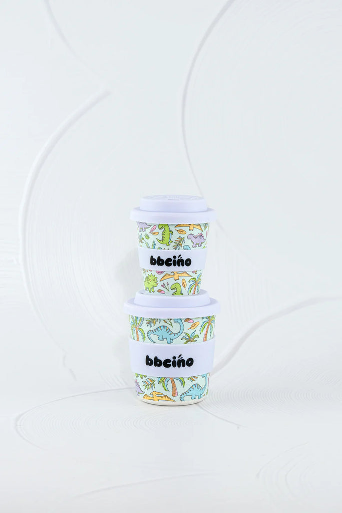 Stack of BBCino reusable cups 240ml in Sipasaurus dinosaur print with white silicone lids, durable and lightweight eco-friendly cups.