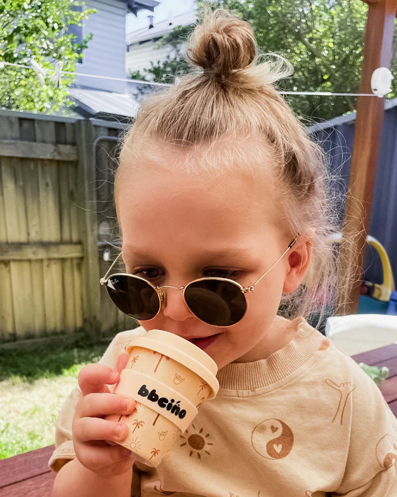 Child drinking from 120ml reusable bamboo cup with neutral palm tree design, perfectly sized for small hands.