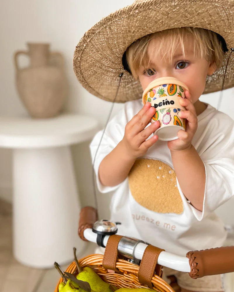 Child drinking from 120ml reusable bamboo cup with tropical fruit design, perfectly sized for small hands.