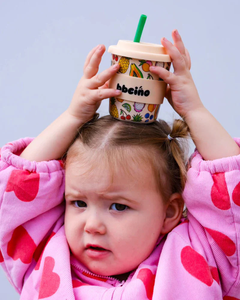 Child balancing 240ml keep cup on head which features a tropical fruit design and green straw