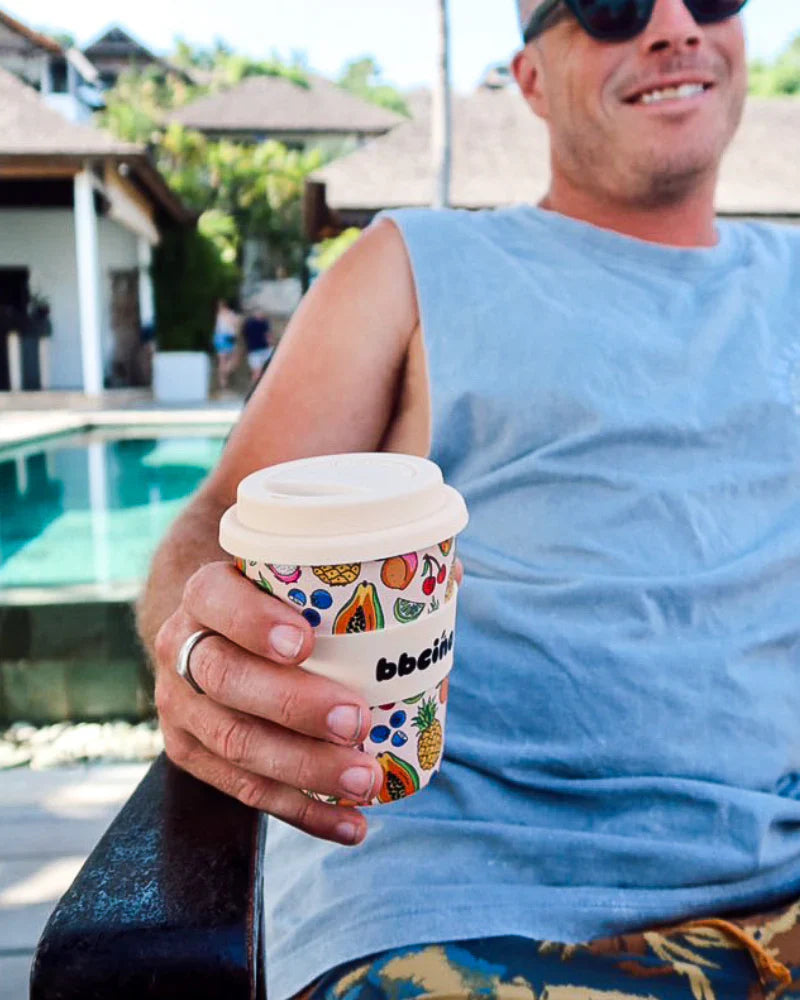 Man holding BiggieCino tropical reusable cup by a pool on a sunny day.