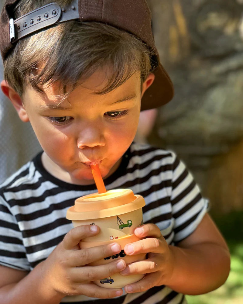 Child drinking from 120ml reusable bamboo cup with orange truck design, perfectly sized for small hands.