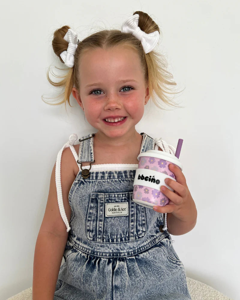 Child smiling and holding a BBCino 240ml reusable cup with purple flowers.