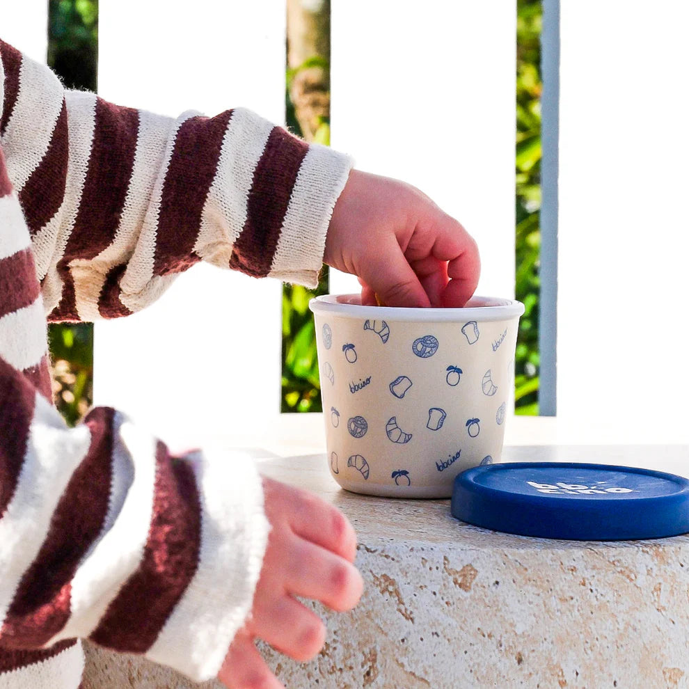 Child reaching into BBCino reusable bamboo snack pot in Brunch-Kins design with navy silicone lid, sustainable and eco-friendly snack container.