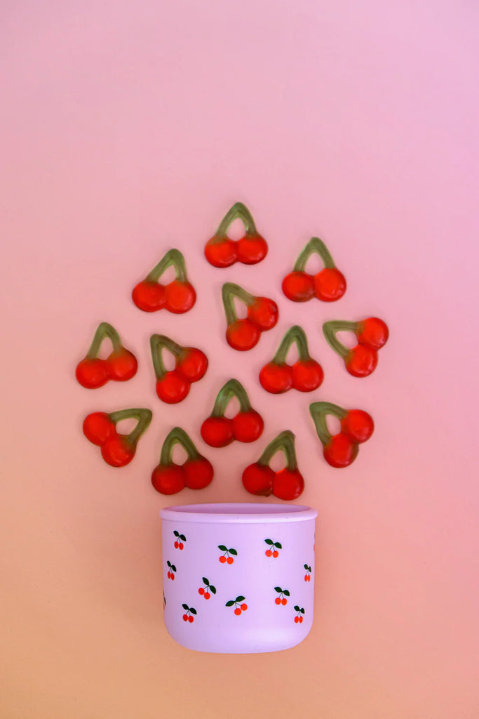 BBCino Cherub silicone snack pot with pink base and cherry print, styled with cherry-shaped lollies on pink background, sustainable snack container.