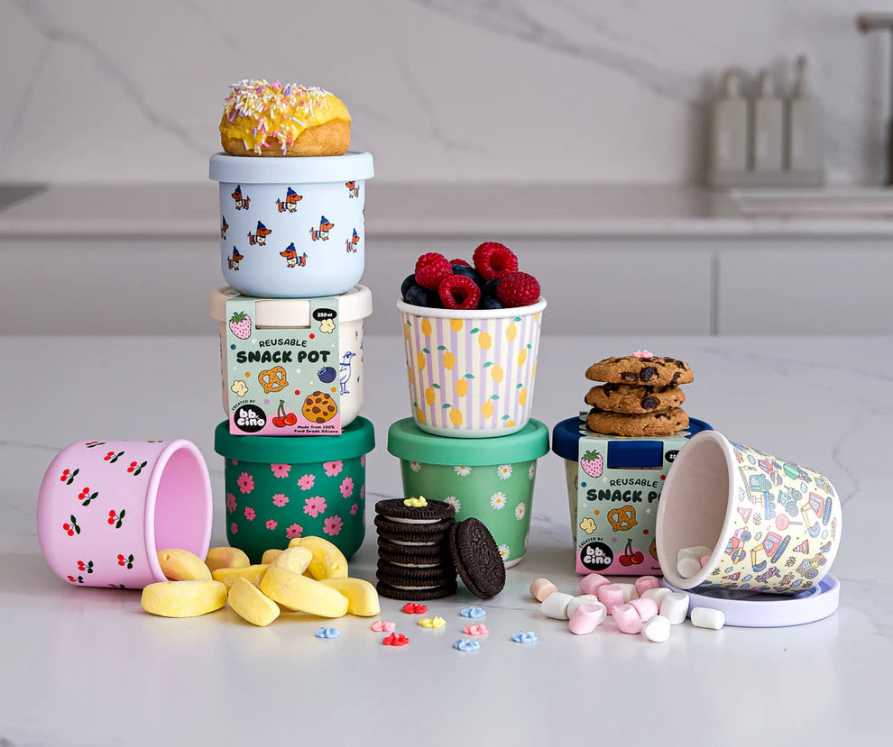 BBCino reusable silicone snack pots in assorted designs including Cherub cherry print, stacked with fruit, biscuits and marshmallows, eco-friendly containers.