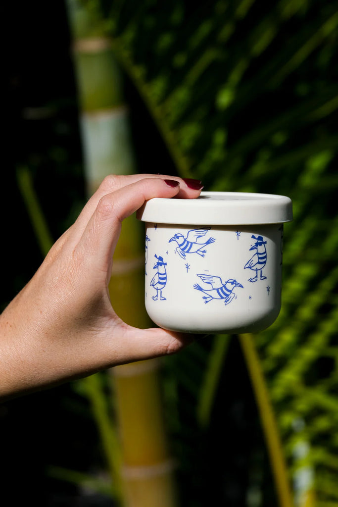 Hand holding BBCino Chippie Crew reusable silicone snack pot with seagull print, sustainable snack container made from 100% food-grade silicone.