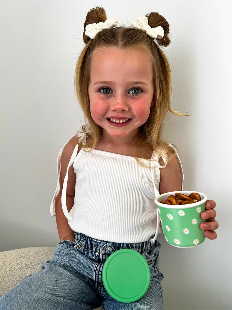 Smiling child holding BBCino reusable bamboo snack pot in Daisy BB green daisy print, eco-friendly and durable container for kids’ snacks.