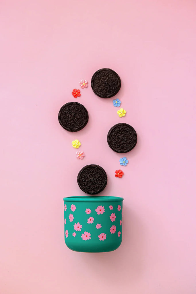 BBCino Ditsy silicone snack pot in green floral design, styled with Oreo cookies and colourful sprinkles on pink background, sustainable reusable container.