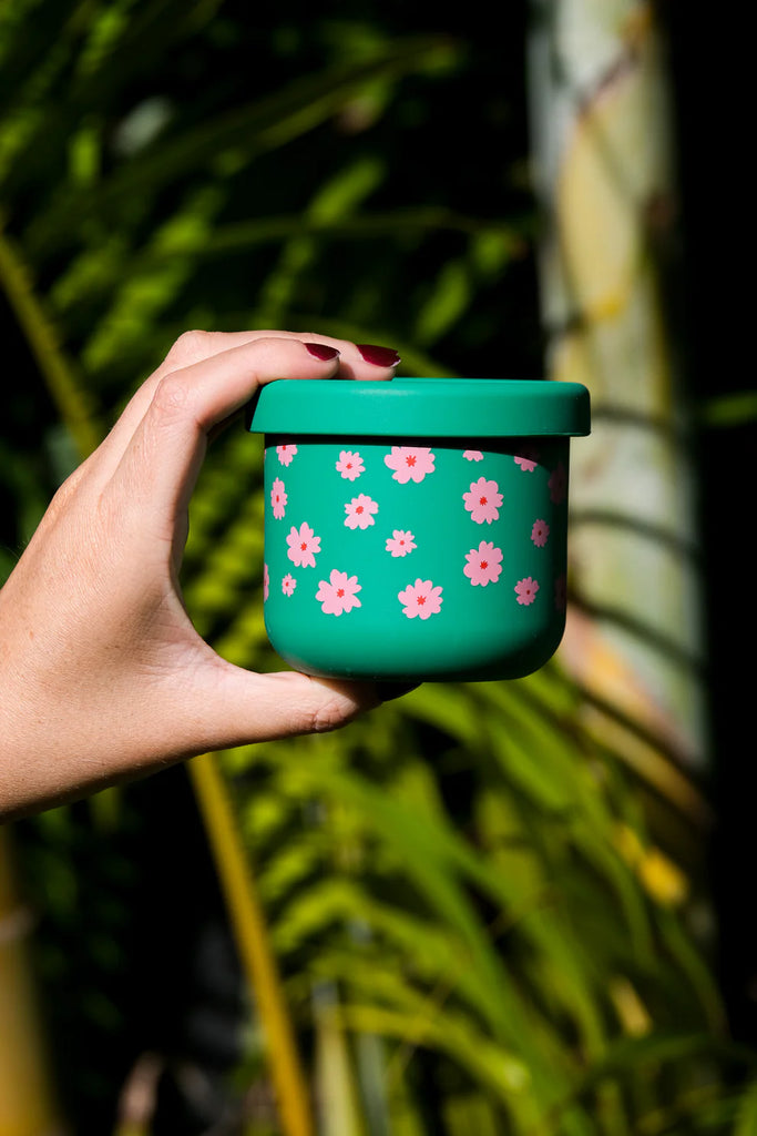 Hand holding BBCino reusable silicone snack pot in Ditsy green floral design with pink flowers, 250ml eco-friendly unbreakable food container.