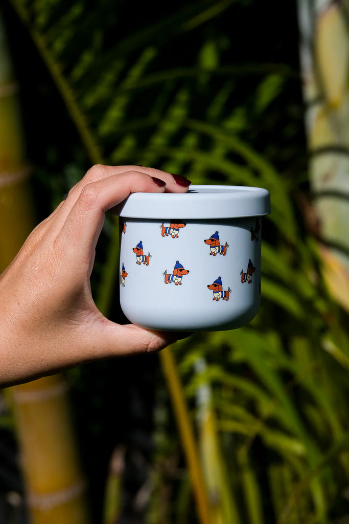 Hand holding BBCino Dagwood silicone snack pot with dachshund dog print and matching lid, eco-friendly reusable container made from food-grade silicone.