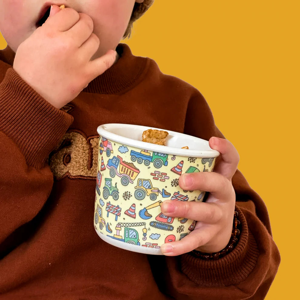 Child eating snacks from BBCino bamboo reusable snack pot in Dig It construction print with silicone lid, eco-friendly sustainable container.