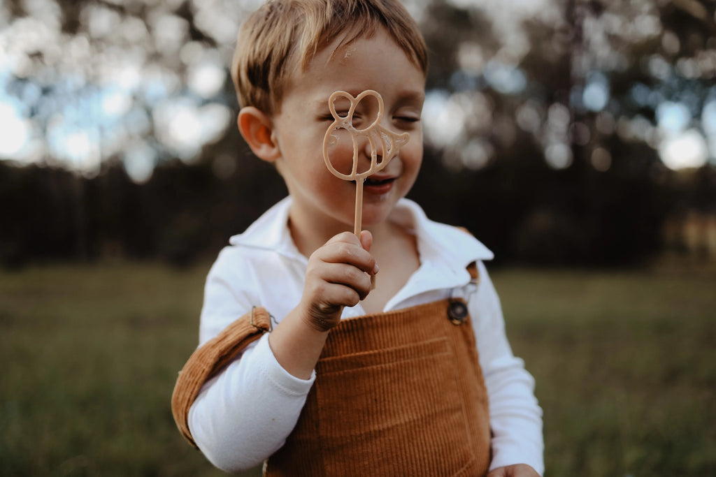Child blowing bubbles using handmade biodegradable bee wand in nature.