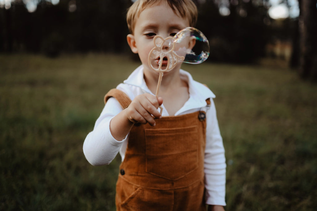 Child playing with eco-friendly bubble wand in grassy field, mid-bubble.