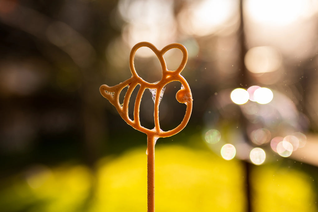 Bee-shaped bubble wand held outdoors by a child in golden sunlight.