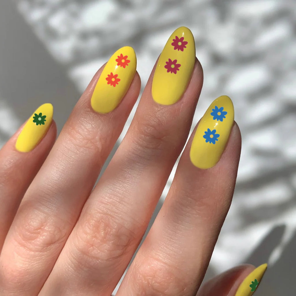 Yellow nails with colorful flower designs on a neutral background