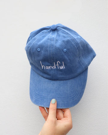 Front view of the "Handful" adults cap in cobalt blue, made from washed 100% cotton, featuring embroidered text and a relaxed, curved brim design.