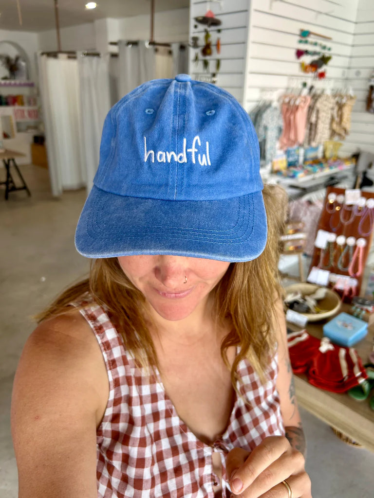 Woman wearing the "Handful" cobalt blue cap indoors, styled casually with a checkered top—showcasing the playful, everyday style of the cap.