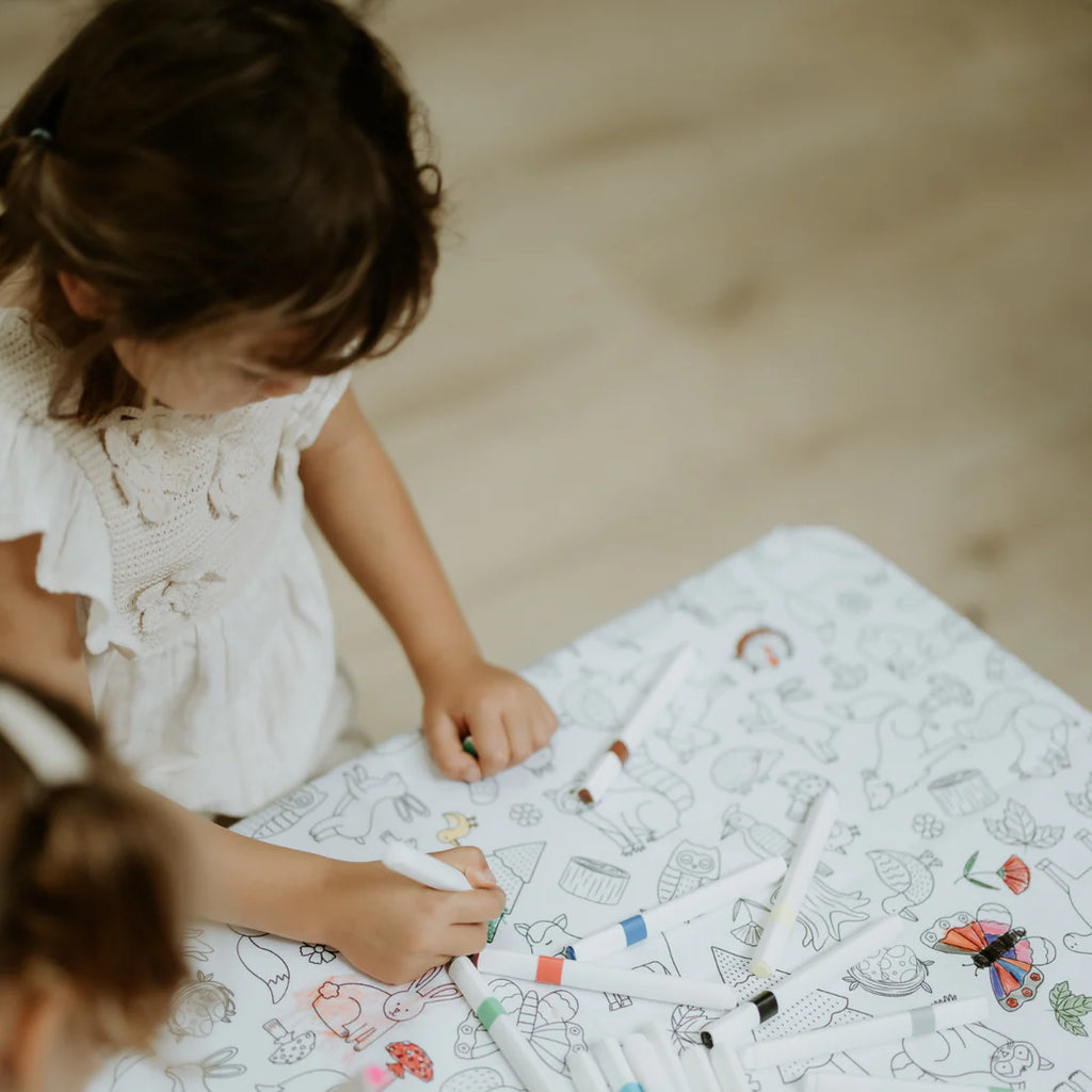 Top-down view of a child enjoying the Woodland Wonders colouring-in tablecloth, demonstrating collaborative, screen-free play at the table.