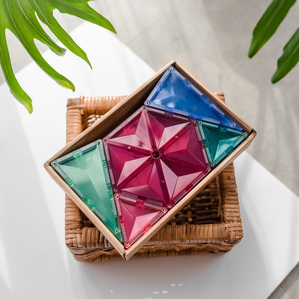 A small wicker basket filled with assembled pastel triangle and hexagon tiles, styled with leaves for a natural, warm feel.