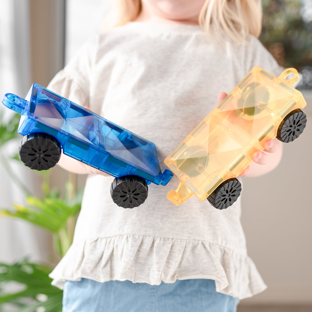 Child holding two completed Connetix cars with blue and yellow motion bases, demonstrating imaginative play.