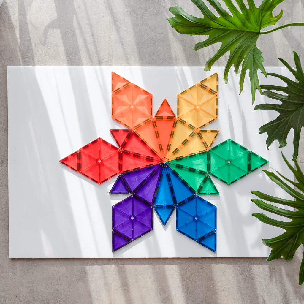 Bright rainbow starburst made from hexagons and triangles in a flat lay, styled with natural light and leafy accents.