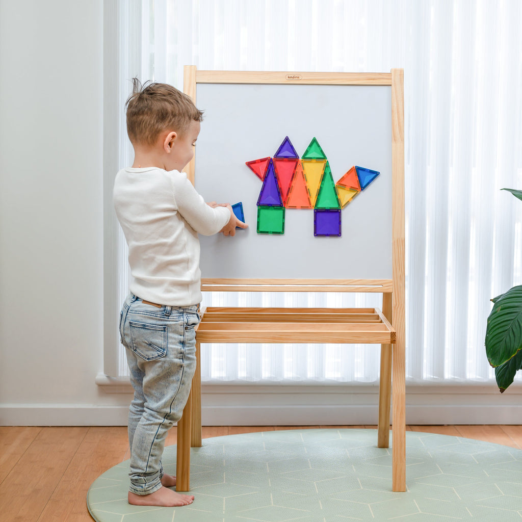Child interacting with magnetic tile creations on a whiteboard easel, featuring a colourful dinosaur shape made from the Rainbow Mini Pack.
