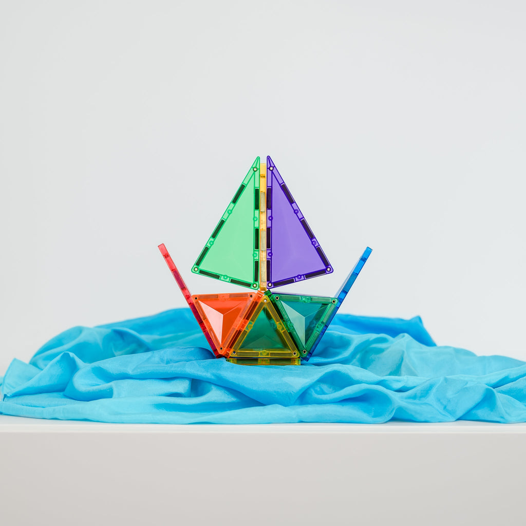 Boat-like 3D structure made with Connetix rainbow tiles displayed on a soft blue cloth for an imaginative play setting.