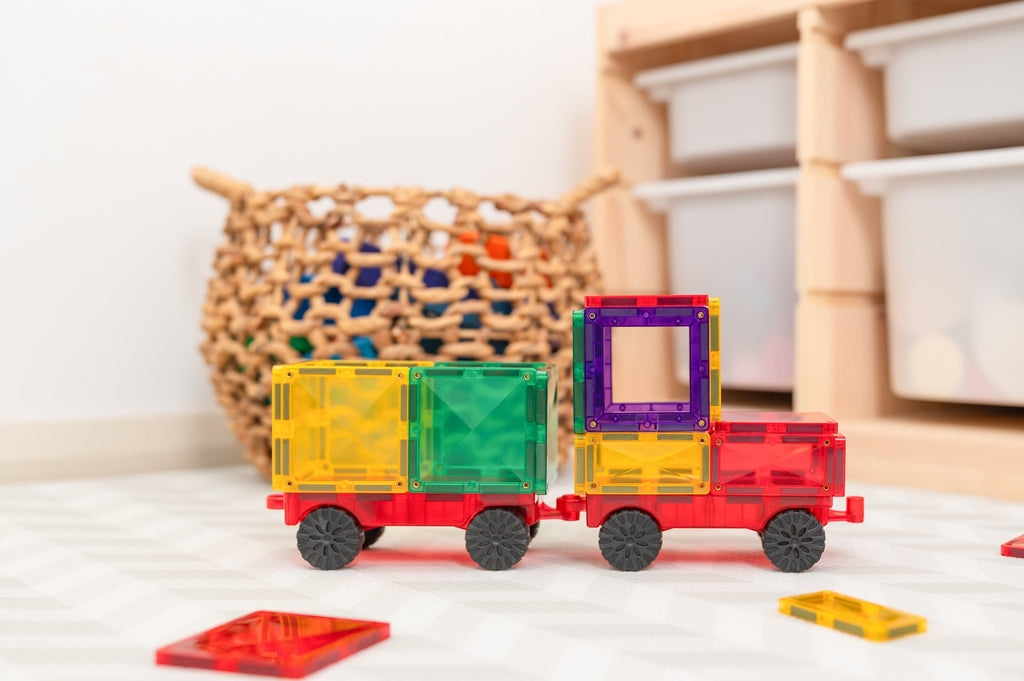 Rainbow tile truck built using the Motion Pack, displayed on the floor near toy storage baskets, showing magnetic construction and rubber wheels.