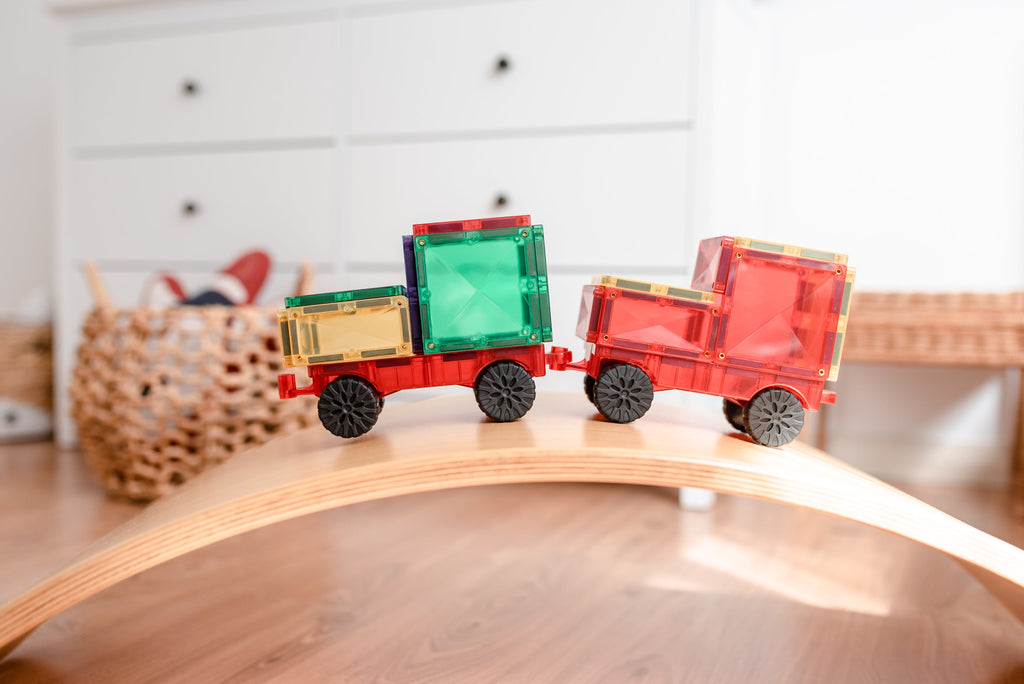 Two colourful vehicle builds from the Motion Pack positioned on a wooden rocker toy, demonstrating movement and balance in play.
