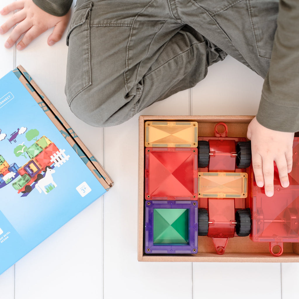 Child’s hand organizing and playing with Connetix Motion Pack tiles neatly arranged inside a wooden tray beside the product box.