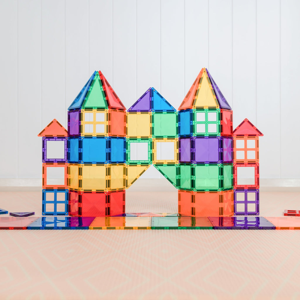 A large, symmetrical building made from Connetix tiles in a rainbow colour scheme, displayed on a light floor with toy baskets nearby.