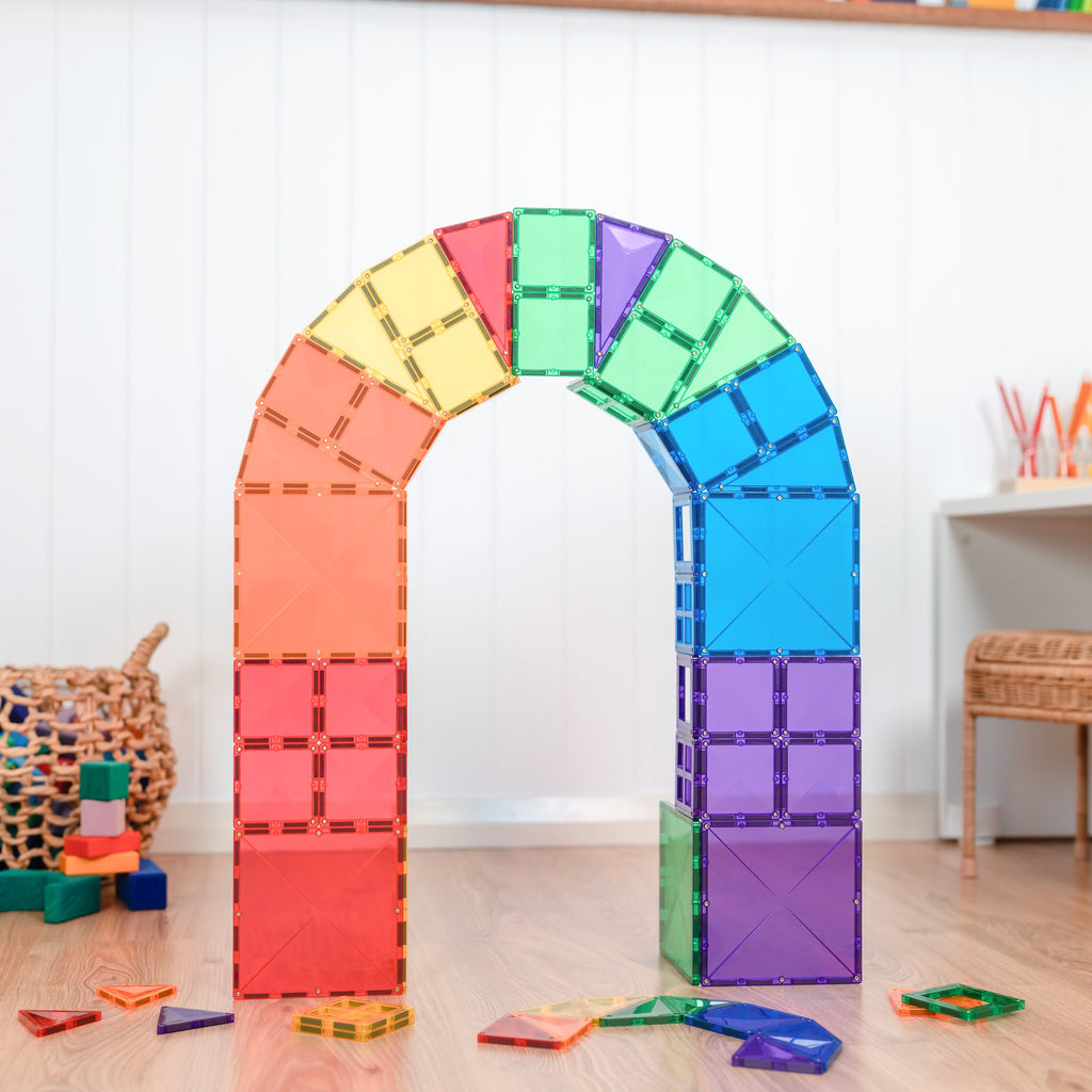 Tall rainbow arch built with magnetic tiles from the Starter Pack, styled in a bright playroom with wooden toys and natural light.