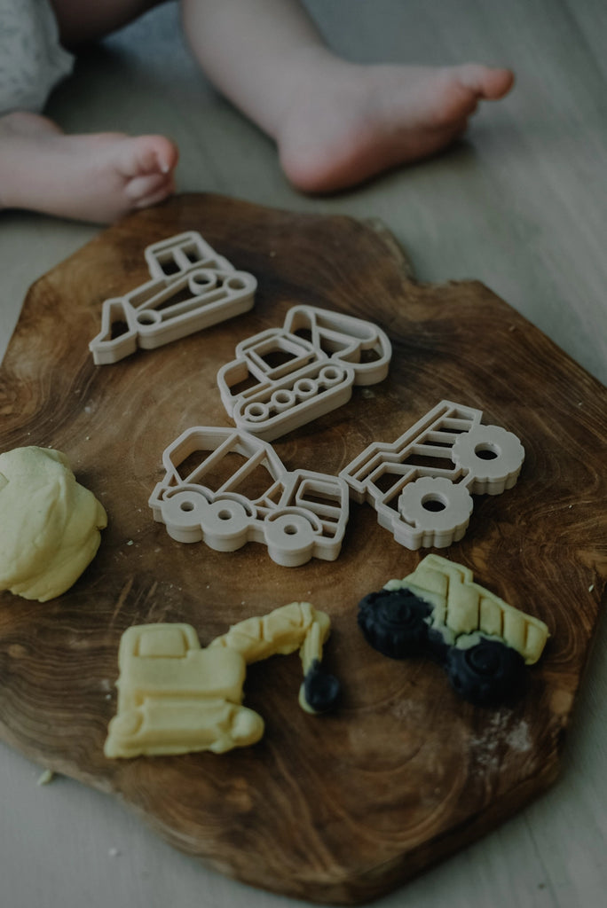 Playdough cutters shaped like Construction vehicles on a wooden board with some playdough cut out and shaped like trucks.
