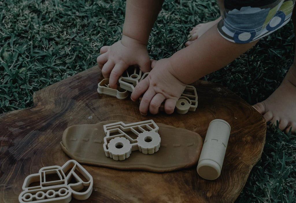 Children playing with playdough cutters on a wooden board outdoors.