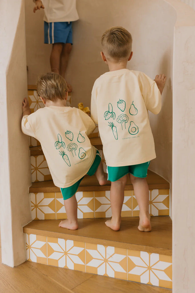 Back view of two children walking upstairs in matching tees, with whimsical green line art and slogan printed on the back, adding fun detail to the outfit.