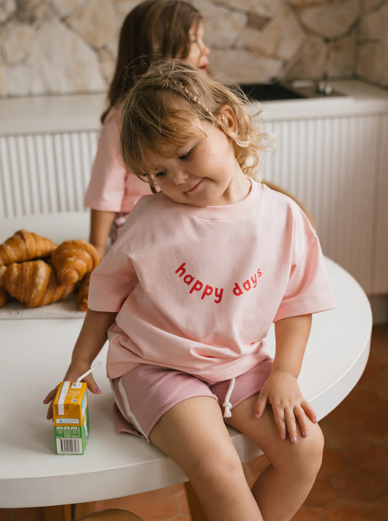 Toddler in pink racer shorts and matching pink tee sitting on a bench with a juice box, highlighting the shorts’ everyday comfort and casual style.