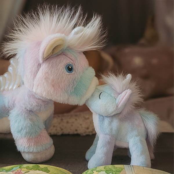 Dazzle unicorn and baby unicorn plush together, kissing – Rainbow pastel unicorn with smaller unicorn companion in a playroom setting.